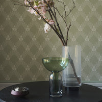 Green and clear glass vases on a black table, against a textured sage green patterned wall.