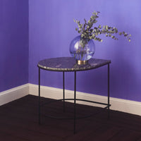 Round marble side table with a sleek black frame, set against a vivid purple wall. Elegant and modern design.