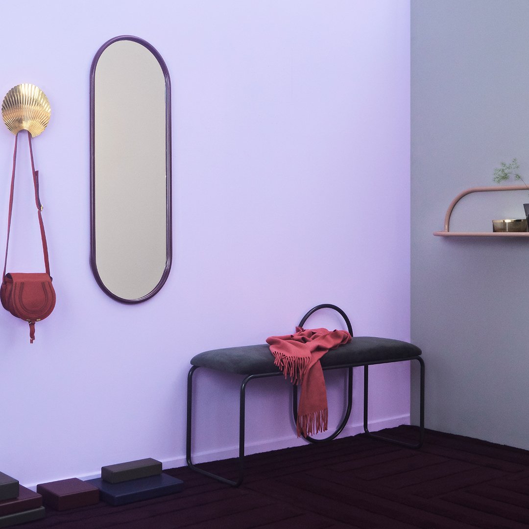 Purple wall with a dark floor and black bench, featuring a red scarf and stylish mirror accents. Modern design elements.
