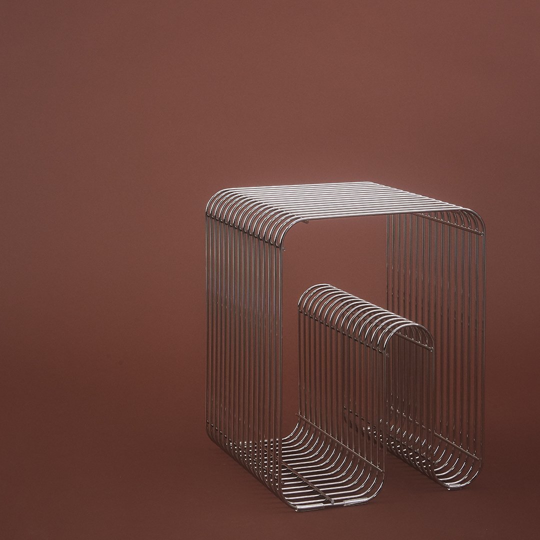 Silver wireframe side table against a warm brown background, featuring a minimalist striped pattern.