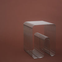 Silver wireframe side table against a warm brown background, featuring a minimalist striped pattern.