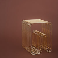 Gold wireframe accent table against a rich brown background, featuring sleek curves and contemporary design.