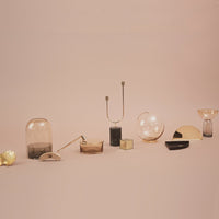 Collection of glass decorative vases in soft amber, clear, and black hues against a pastel pink background.