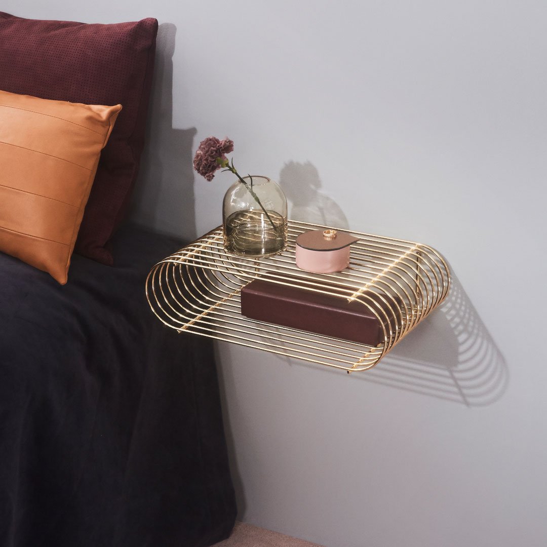 Gold wire wall shelf with a sleek, modern design; soft textures of dark gray and vibrant copper cushions in background.