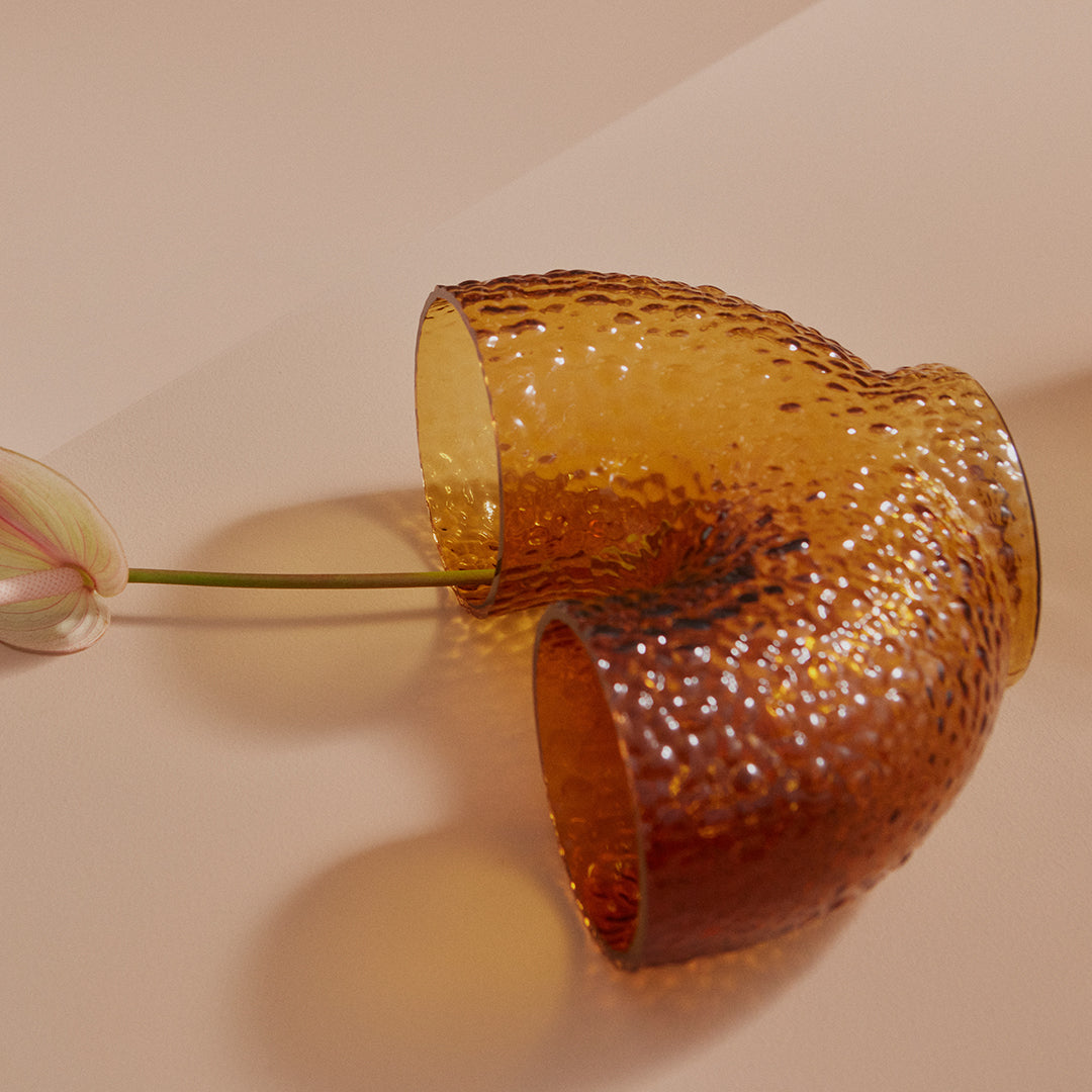 Amber glass vase with a textured, dimpled pattern, set against a soft pink background.