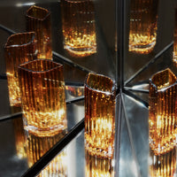 Amber glass vases with textured stripes reflecting light on a mirrored surface. Elegant and modern design.