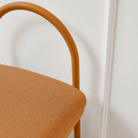 Stylish orange chair with a textured fabric seat and curved, polished metal legs against a white background.