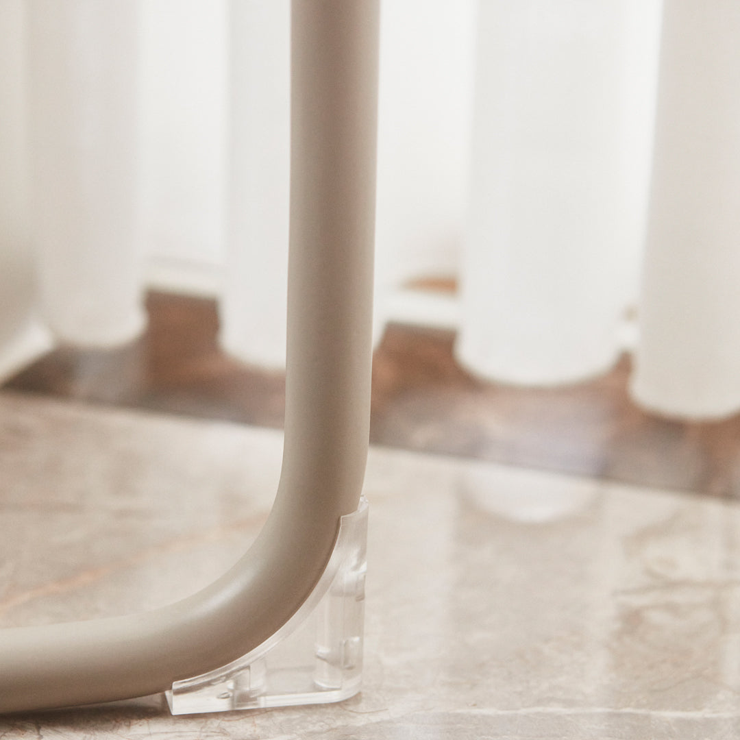 Elegant beige tubing with clear acrylic base, set against soft white curtains and a patterned marble floor.