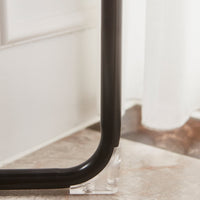 Black metal frame with clear acrylic accent, set against a light stone floor and white curtain backdrop.