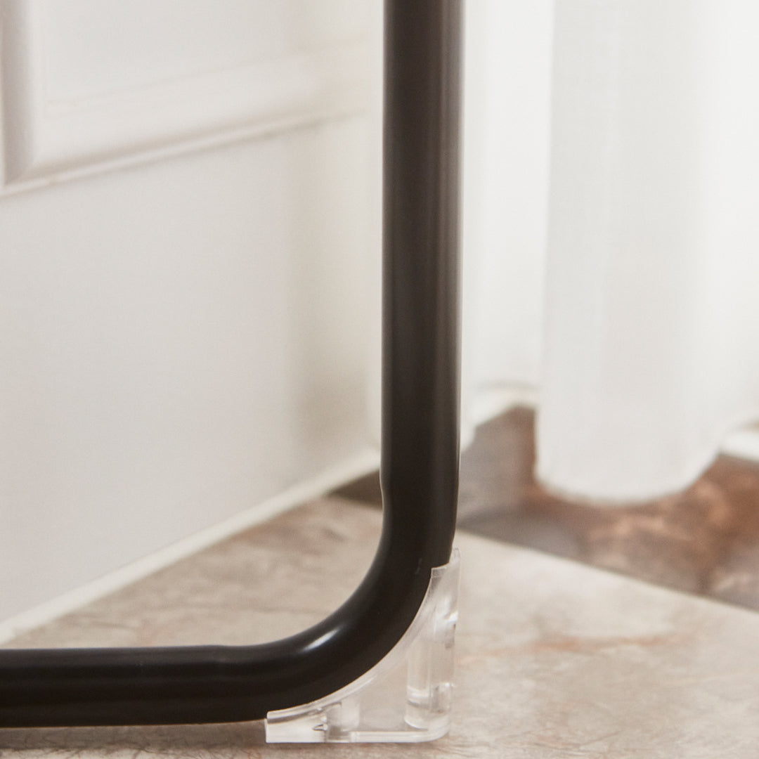 Black curved metal frame with clear acrylic support against a light-colored floor. Subtle textures and shadows visible.