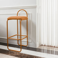 Orange upholstered bar stool with a minimalist metal frame against a neutral backdrop. Modern design with geometric shapes.