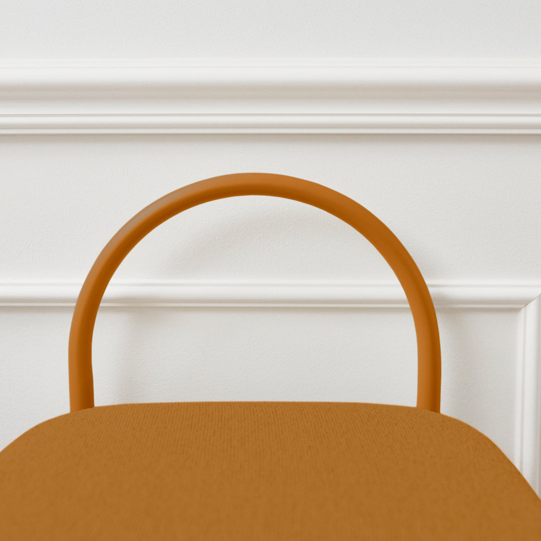 Rust-colored chair with a smooth fabric seat and a rounded orange handle against a white wall.