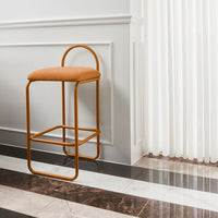 Orange upholstered bar stool with sleek metal frame, set against a patterned dark and light tiled floor.