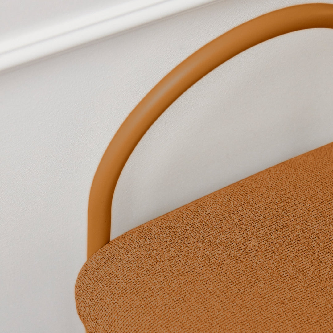 Rust-orange seat with a smooth, textured fabric and a matching curved handle against a neutral background.
