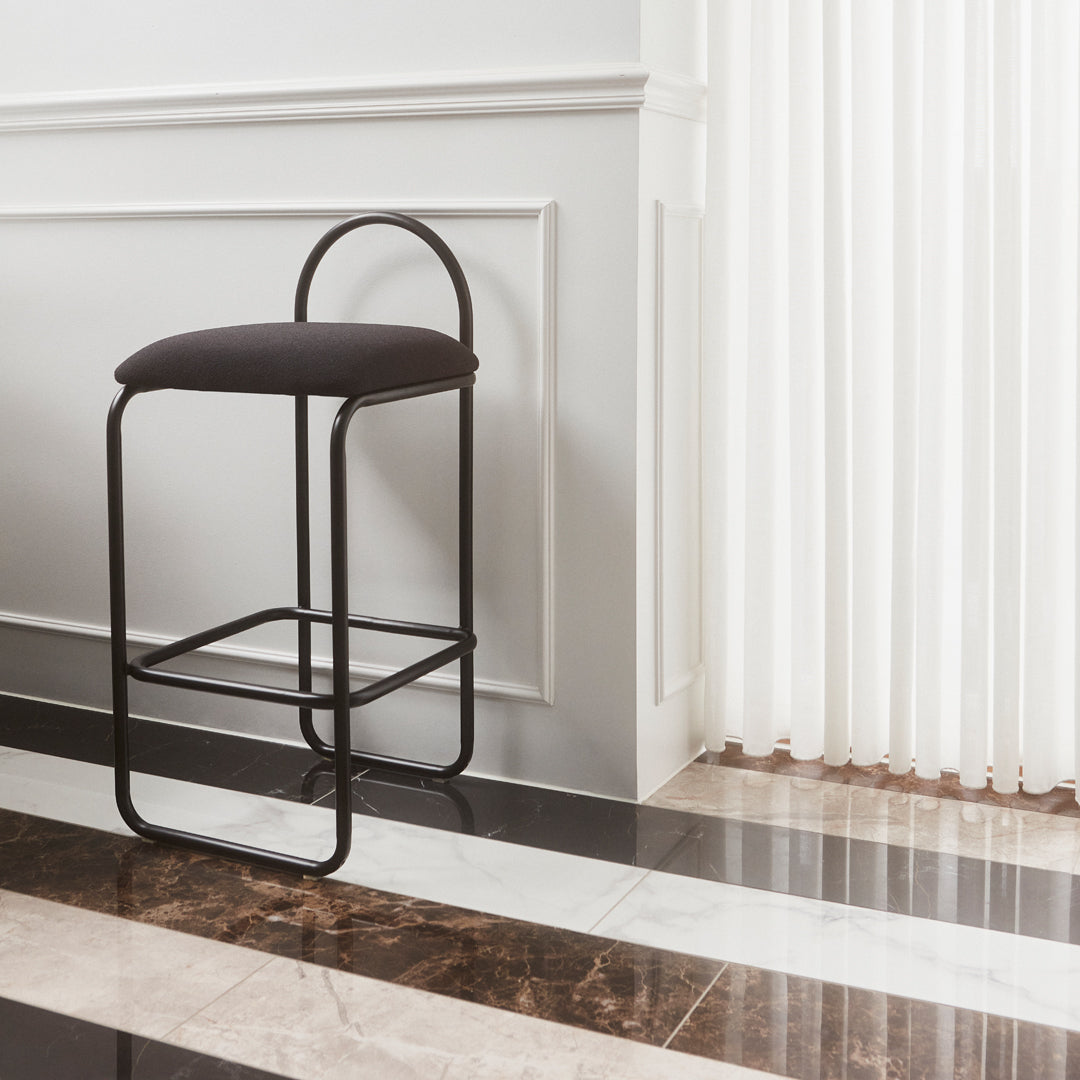 Modern black metal bar stool with a textured dark fabric seat against a sleek marble-style floor.