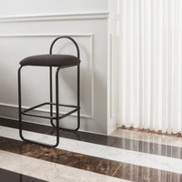 Modern black metal bar stool with a textured dark fabric seat against a sleek marble-style floor.