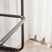 Black metal frame with sleek lines, contrasting against a light, airy white curtain and polished stone floor.
