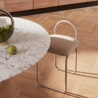 Beige upholstered chair with a sleek white metal frame, set against a marble table and warm wood flooring.