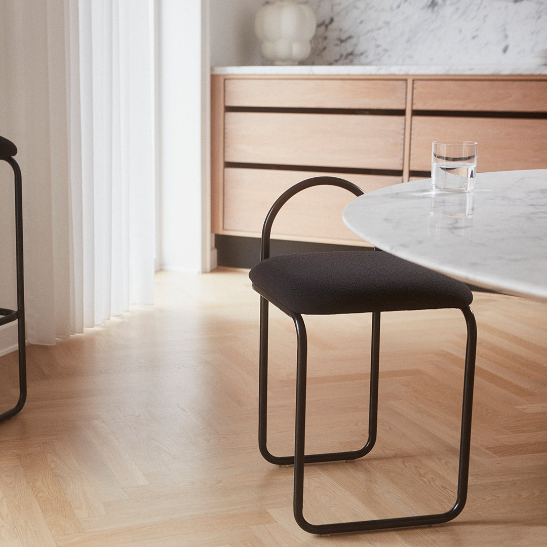 Black upholstered chair with a minimalist design, featuring sleek metal legs, set against a warm wood floor and light marble.