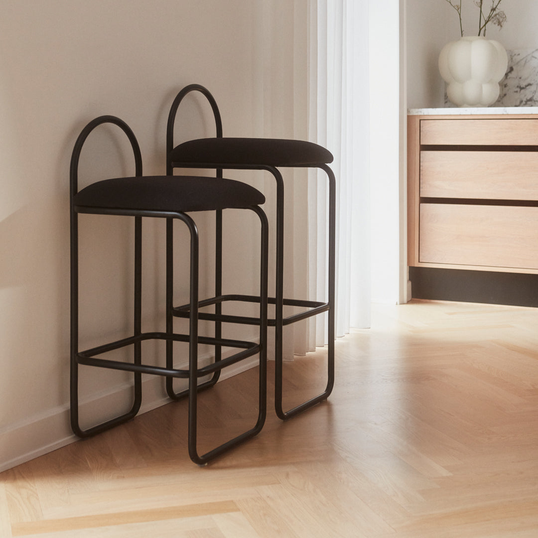Black metal bar stools with circular backs and a minimalist design, featured on a light wood floor.