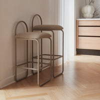 Two beige bar stools with curved backs on a light wood floor, featuring a minimalist design and neutral tones.