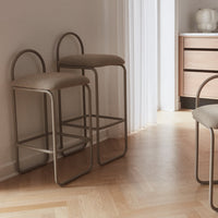 Set of two neutral-colored bar stools with minimalist metallic frames and soft beige cushions, featuring a sleek, modern design.