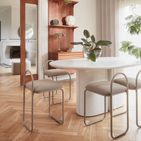 Light beige chairs with curved metal frames around a white round table in a warm-toned, modern dining room.