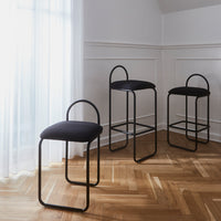 Black upholstered bar stools with minimalist design and sleek metal frames on a herringbone wooden floor.