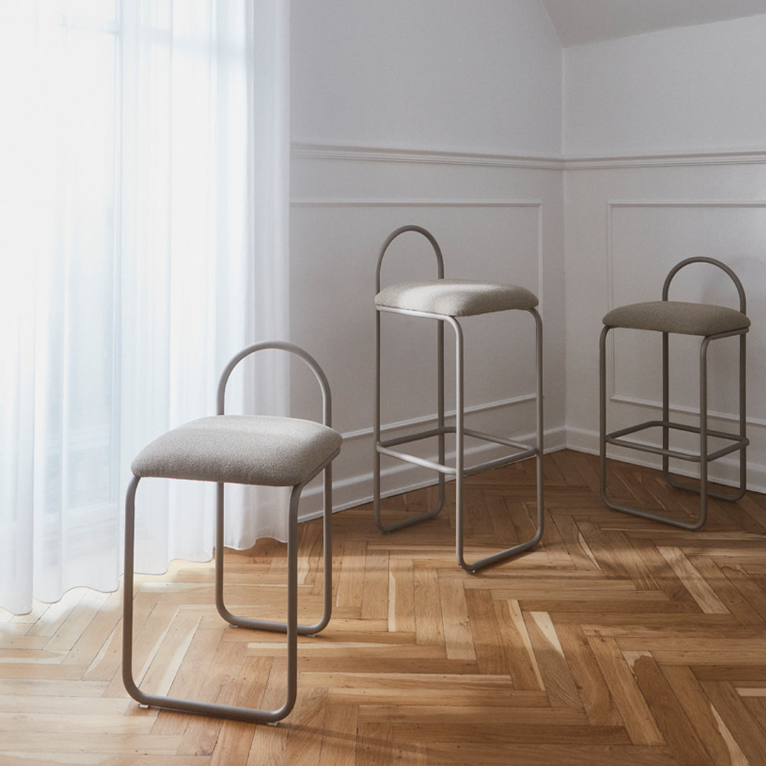 Three modern bar stools with beige upholstery and minimalist metal frames, set against a light-filled, hardwood floor.