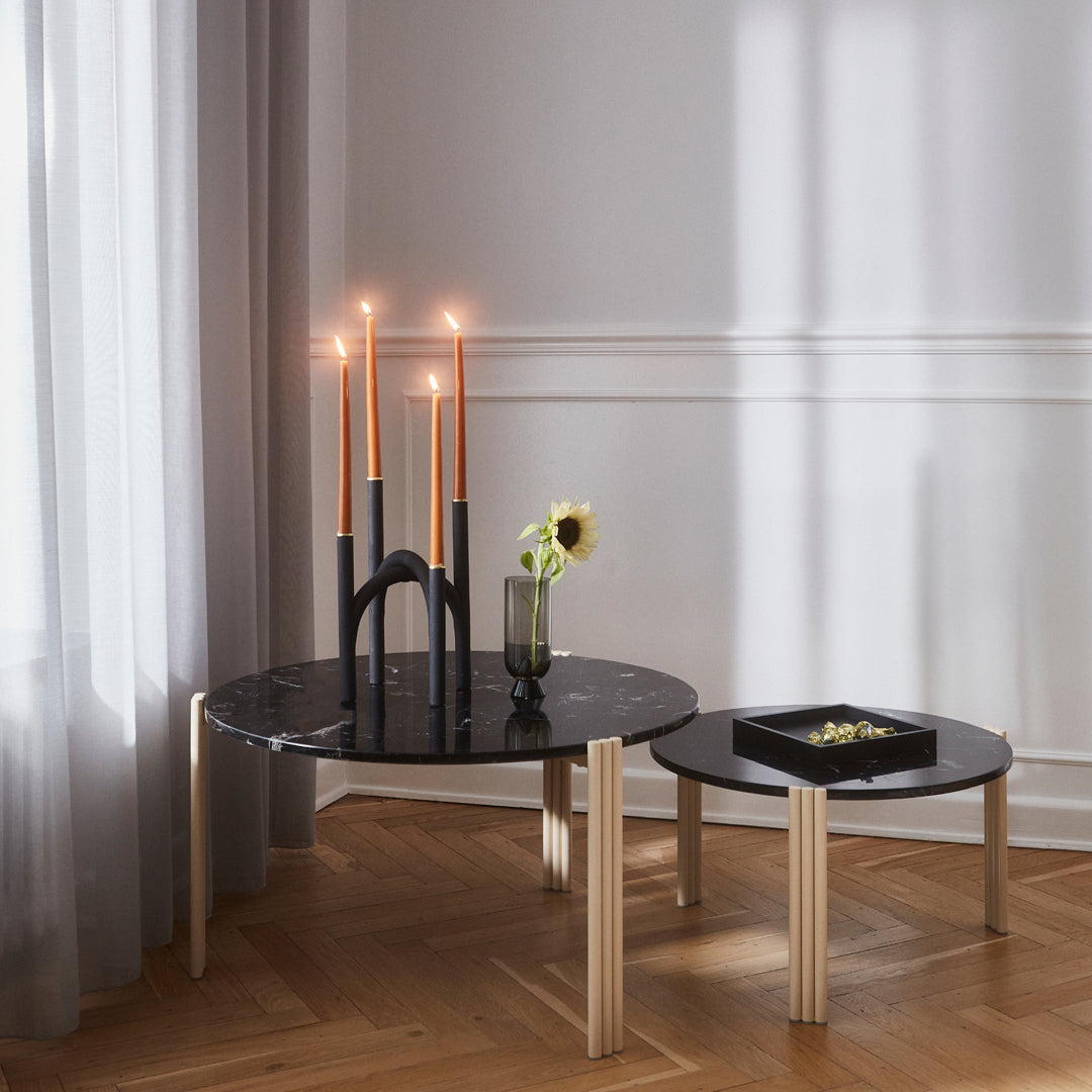 Black marble coffee table with elegant gold-tone wooden legs and a minimalist design, accented by tall black candle holders.