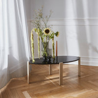 Black oval coffee table with wooden legs, featuring a smooth surface and complemented by a floral arrangement.