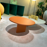 "Round orange coffee table on soft beige carpet, surrounded by green and yellow decor elements."