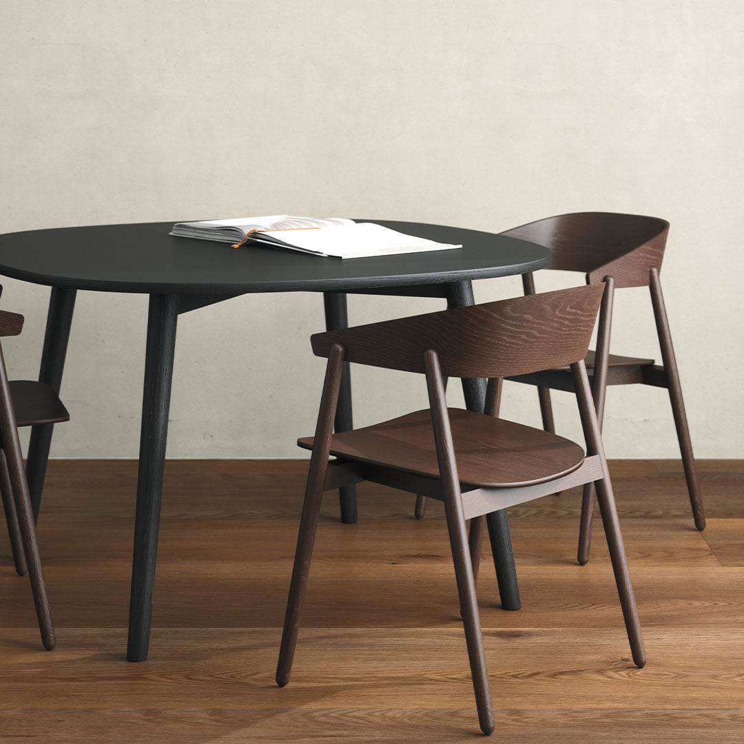 Modern black round table with dark wood chairs on light wood floor, featuring sleek lines and natural textures.