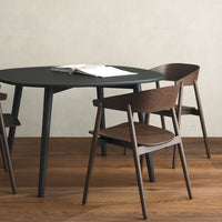 Modern black round table with dark wood chairs on light wood floor, featuring sleek lines and natural textures.