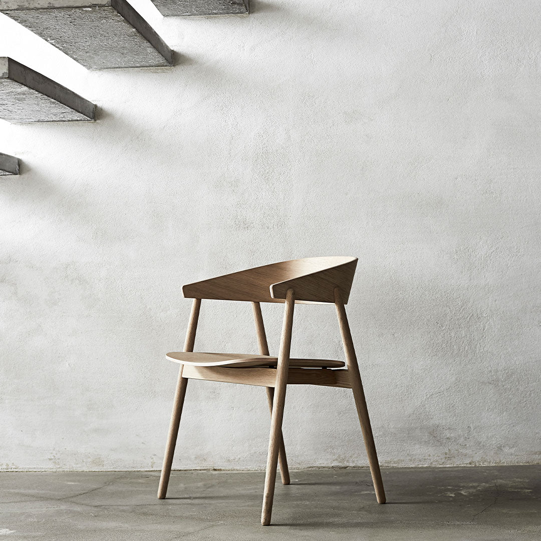 Modern wooden chair in natural beige tones, featuring sleek lines and minimalist design against a white wall.