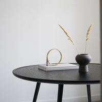 Black round table with a textured surface, featuring minimalist decor in neutral tones and golden accents.