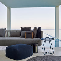 Modern outdoor lounge area featuring gray upholstery, dark cushions, a navy pouf, and a black striped rug.