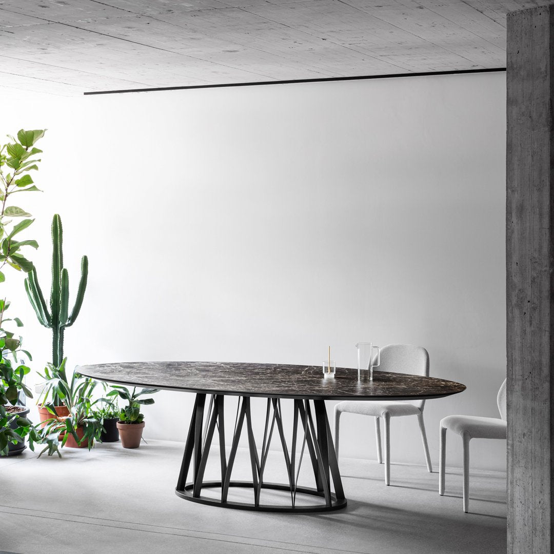 "Round wooden dining table with a dark, textured top and geometric black metal base, set against a minimalist white background."