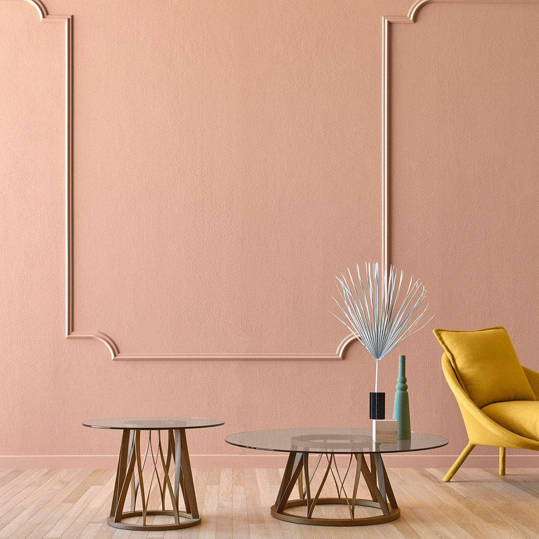 Stylish glass coffee tables with airy geometric bases, set against a soft coral wall and accented by a vibrant yellow chair.