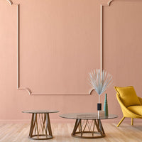 Stylish glass coffee tables with airy geometric bases, set against a soft coral wall and accented by a vibrant yellow chair.