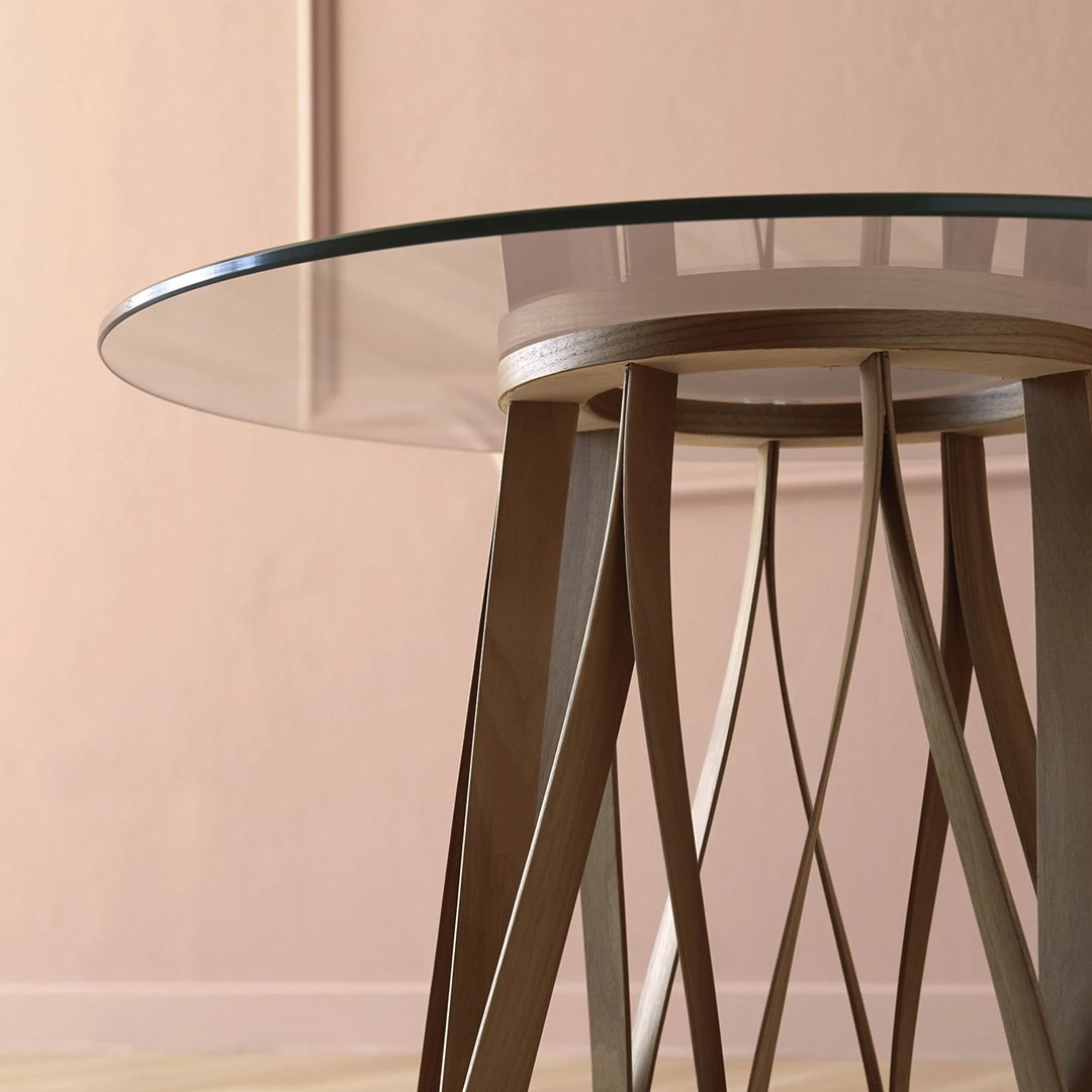 Glass-top table with a geometric wooden base in warm brown tones against a soft pink background.