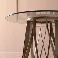 Glass-top table with a geometric wooden base in warm brown tones against a soft pink background.