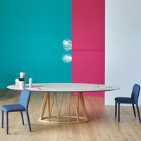 Round dining table with a light gray top, surrounded by navy blue chairs, against vibrant teal and pink walls.