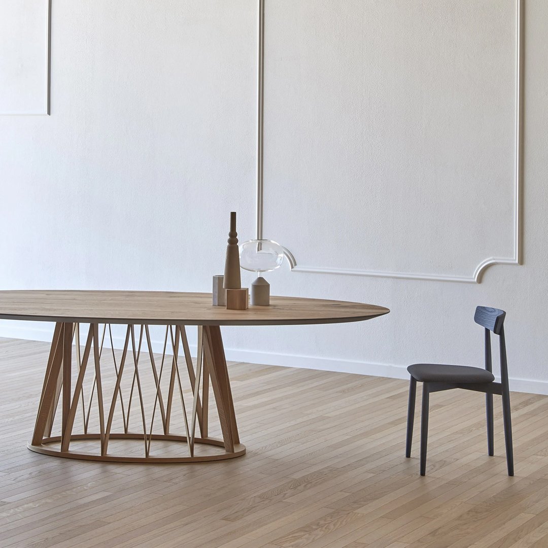 Wooden oval dining table with a textured natural finish, paired with a sleek dark gray chair and minimalistic decor.