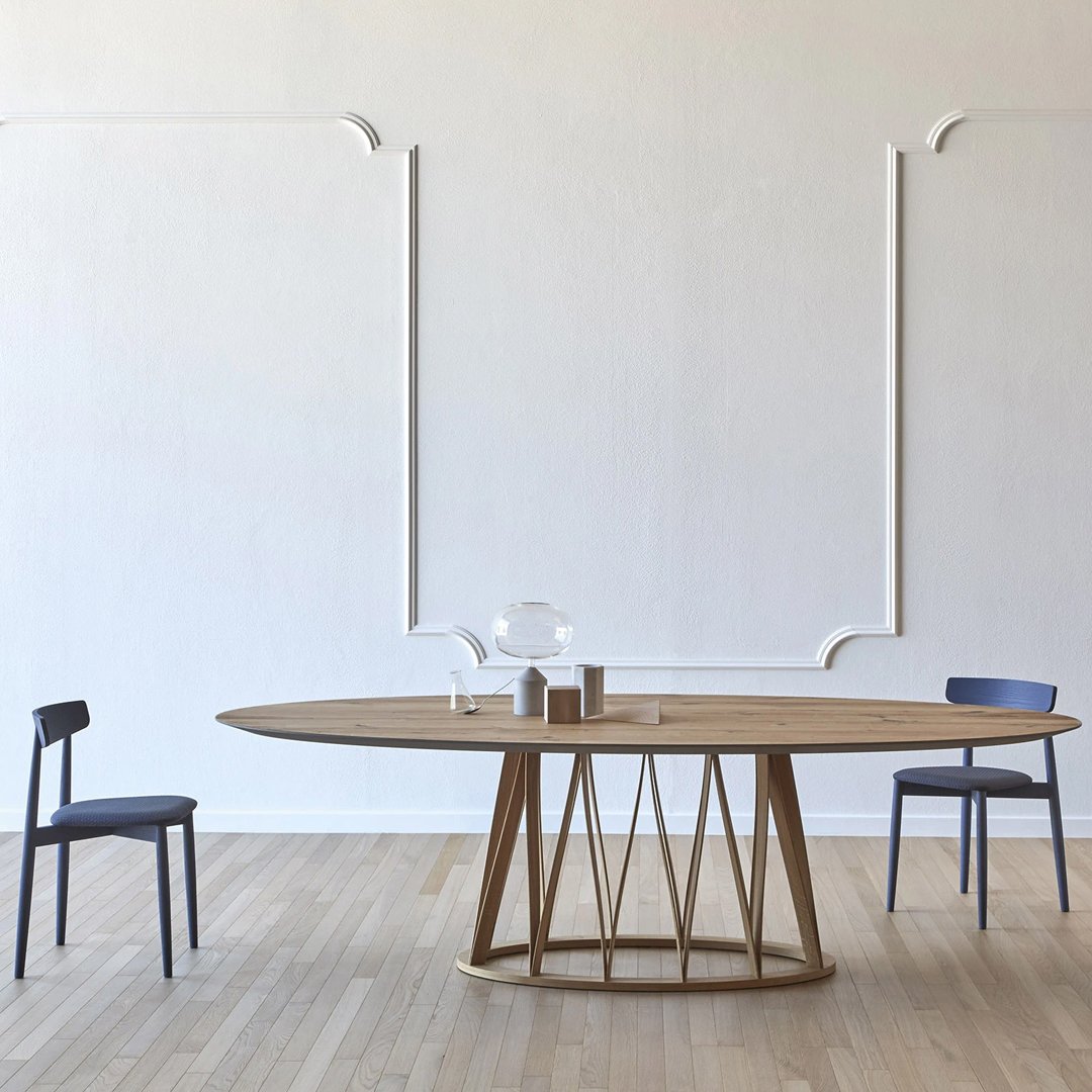 "Oval wooden dining table with natural finish, complemented by dark blue chairs against a light-colored wall."