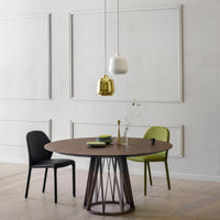 Round wooden dining table with modern black and green chairs, accented by minimalist gold and white pendant lights.
