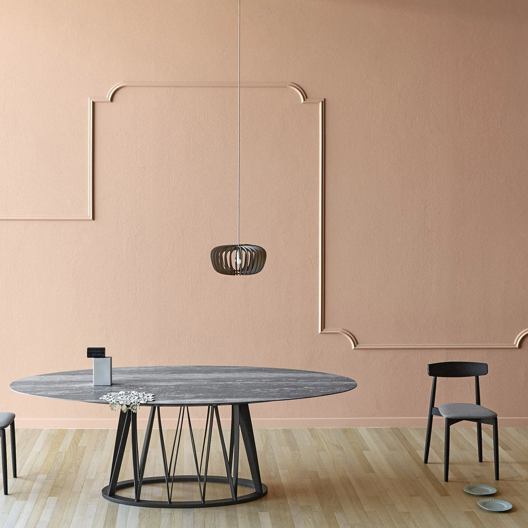 Modern oval table with a gray wood finish, black metal base, set against a soft peach wall, featuring minimalist decor.