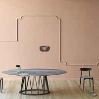 Modern oval table with a gray wood finish, black metal base, set against a soft peach wall, featuring minimalist decor.
