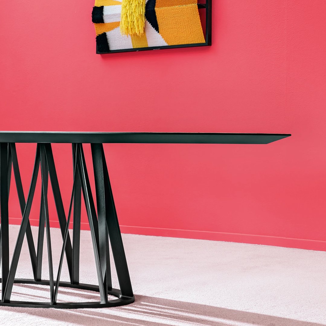 Stylish black table with geometric base, against vibrant pink wall and colorful abstract art. Perfect modern decor.