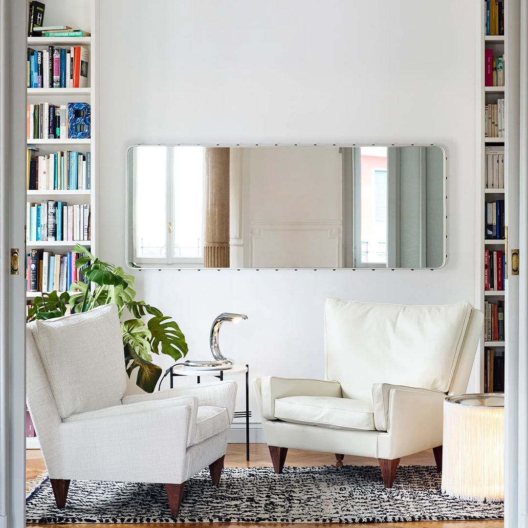 Modern white armchairs with wooden legs on a black and white geometric rug, surrounded by greenery and a mirrored wall.